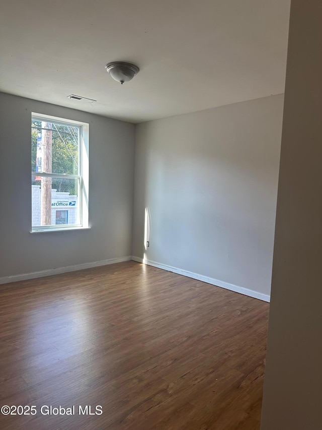 empty room with dark wood-style flooring, baseboards, and visible vents