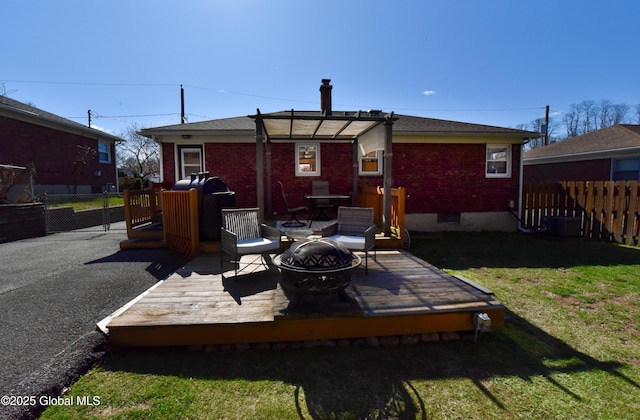 back of house featuring a wooden deck, brick siding, fence, a yard, and a fire pit