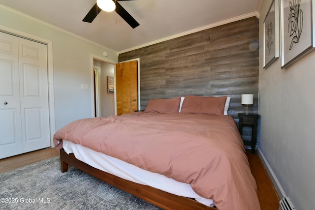 bedroom featuring ceiling fan, wood walls, wood finished floors, a baseboard heating unit, and ornamental molding