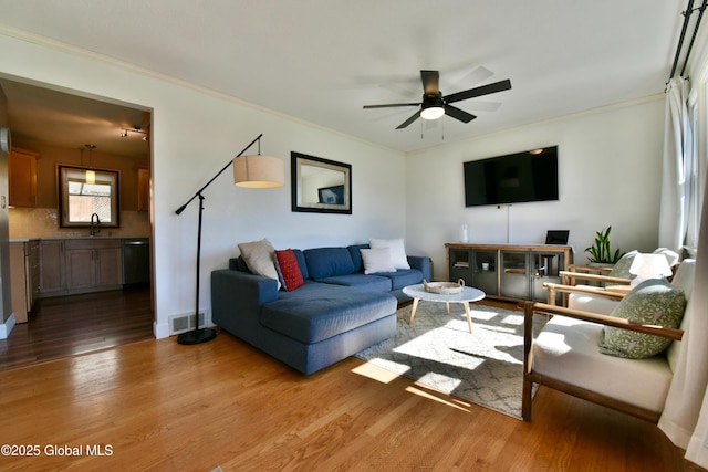 living room featuring ceiling fan, visible vents, ornamental molding, and light wood-style floors