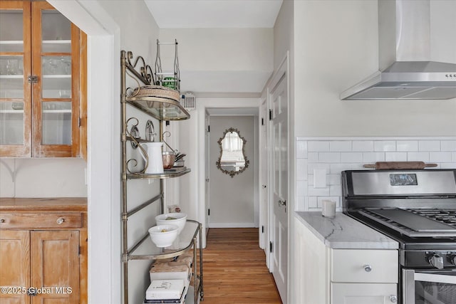 39 5th Ave, Saratoga Springs, NY 12866 - kitchen featuring wall chimney range hood, gas range, light wood-type flooring, glass insert cabinets, and light stone countertops