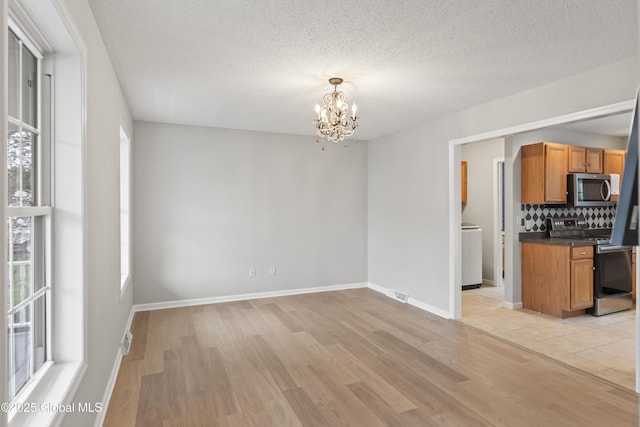 interior space featuring visible vents, washer / dryer, baseboards, a chandelier, and light wood finished floors