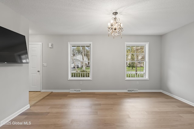 interior space with visible vents, a healthy amount of sunlight, an inviting chandelier, and light wood-style floors