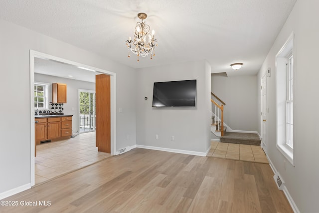 unfurnished living room featuring stairway, visible vents, light wood finished floors, and a chandelier