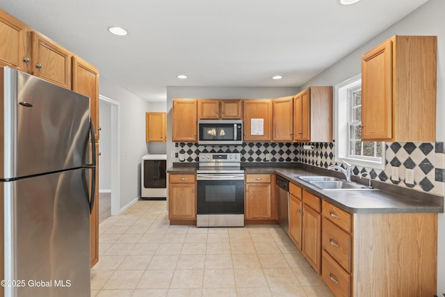 kitchen with dark countertops, appliances with stainless steel finishes, a sink, washer / clothes dryer, and tasteful backsplash