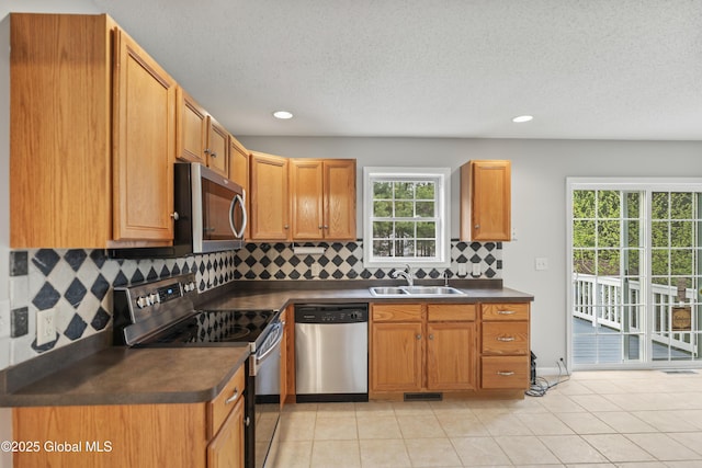 kitchen featuring a sink, appliances with stainless steel finishes, a healthy amount of sunlight, and dark countertops