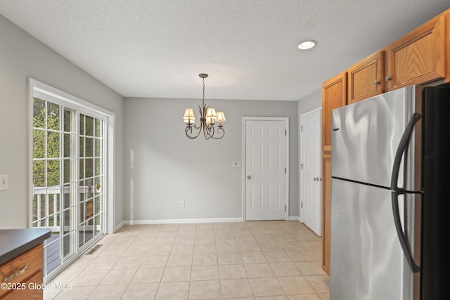 kitchen featuring brown cabinets, a textured ceiling, a chandelier, freestanding refrigerator, and baseboards