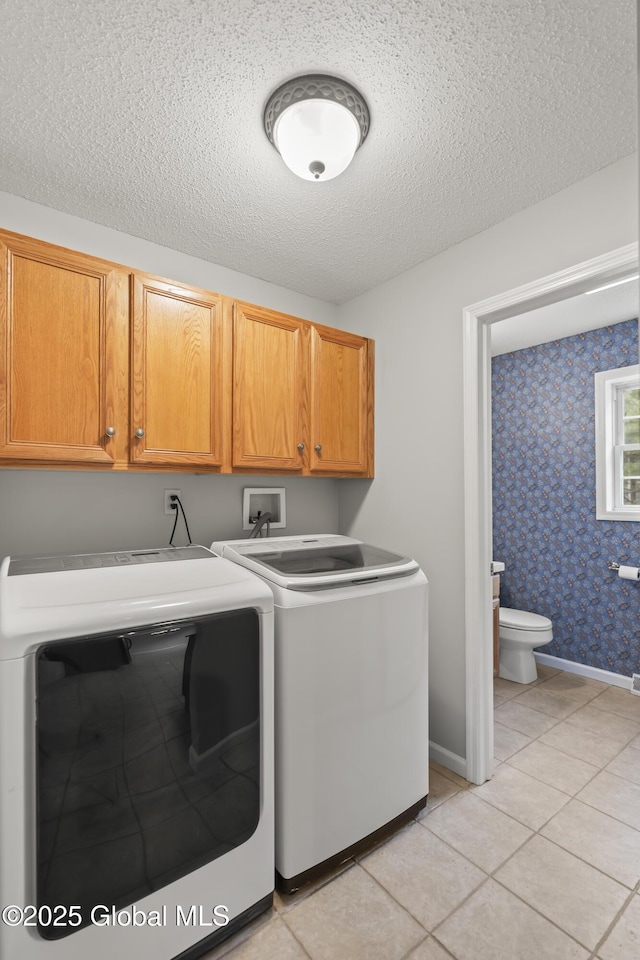 laundry room featuring a textured ceiling, light tile patterned flooring, cabinet space, and washer and dryer