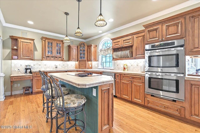 kitchen featuring brown cabinets, tile countertops, appliances with stainless steel finishes, and light wood-style floors