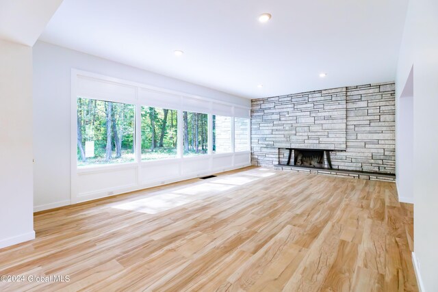 unfurnished living room featuring wood finished floors, visible vents, baseboards, and a stone fireplace
