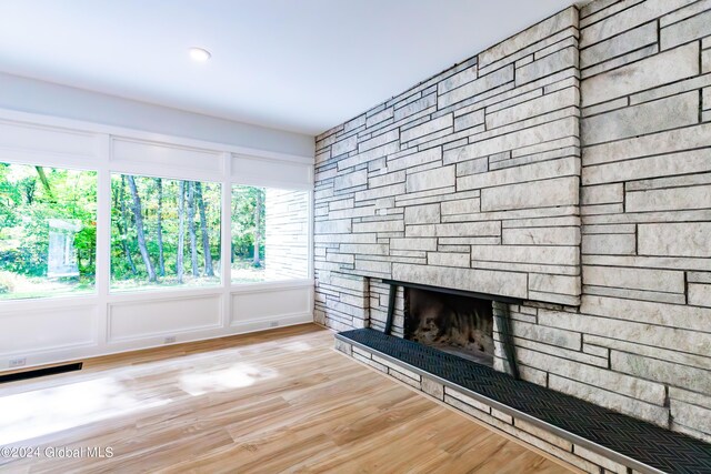 unfurnished living room with visible vents, a stone fireplace, and wood finished floors