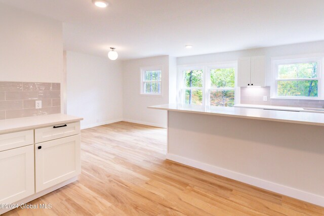 kitchen featuring tasteful backsplash, light countertops, white cabinets, and light wood-type flooring