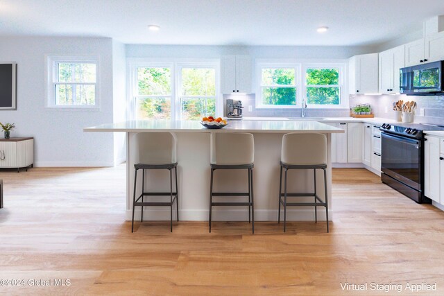 kitchen featuring white cabinets, stainless steel microwave, black / electric stove, and a breakfast bar