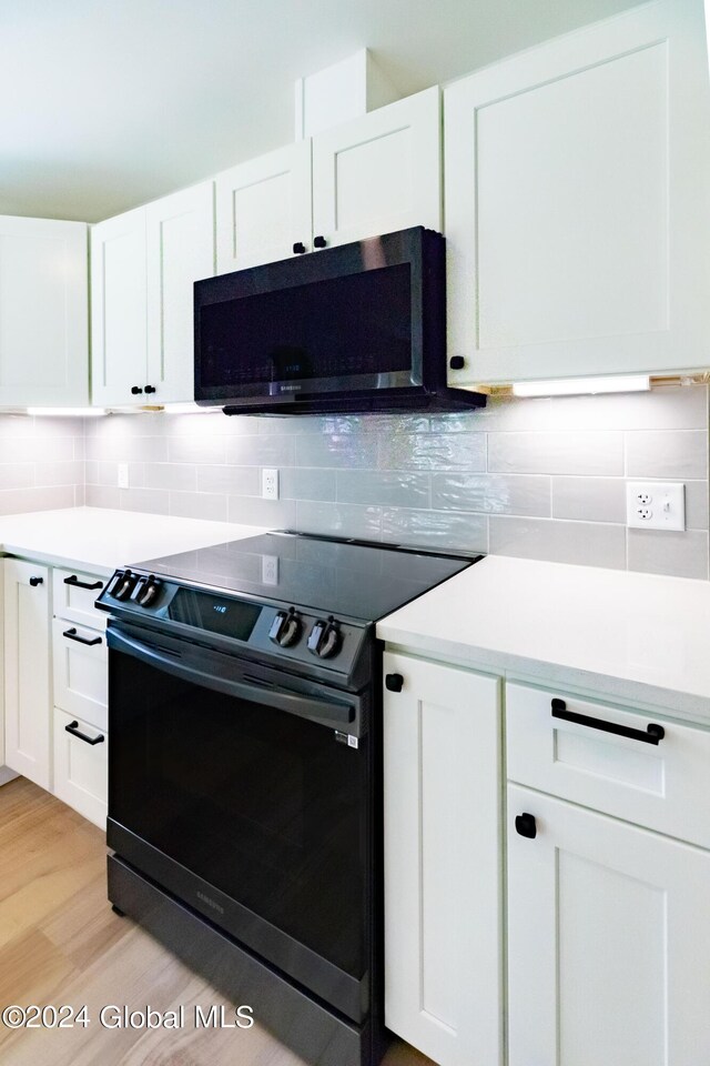 kitchen with black range with electric stovetop, light countertops, backsplash, and white cabinets