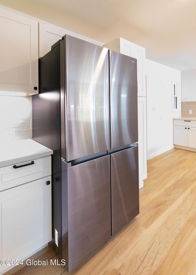 kitchen featuring freestanding refrigerator, light wood-style flooring, white cabinetry, light countertops, and decorative backsplash