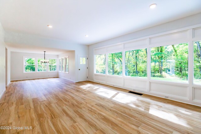spare room with visible vents, light wood finished floors, plenty of natural light, and a notable chandelier