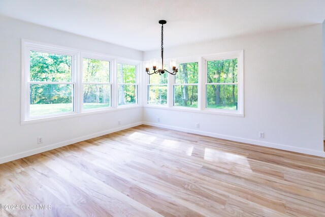 unfurnished room with a notable chandelier, baseboards, and light wood-style flooring