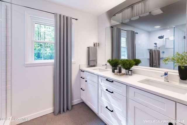 full bath with double vanity, a tile shower, baseboards, and a sink