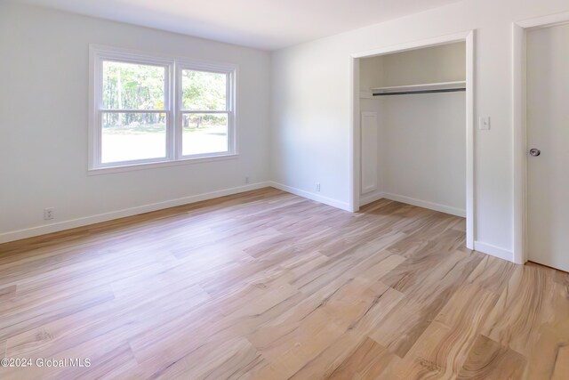 unfurnished bedroom featuring light wood-style flooring, a closet, and baseboards