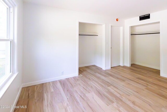 unfurnished bedroom featuring multiple closets, light wood-style floors, and baseboards