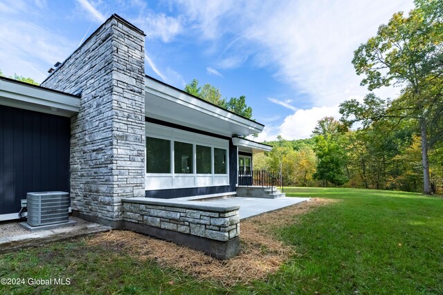 exterior space with a chimney, stone siding, a lawn, and cooling unit