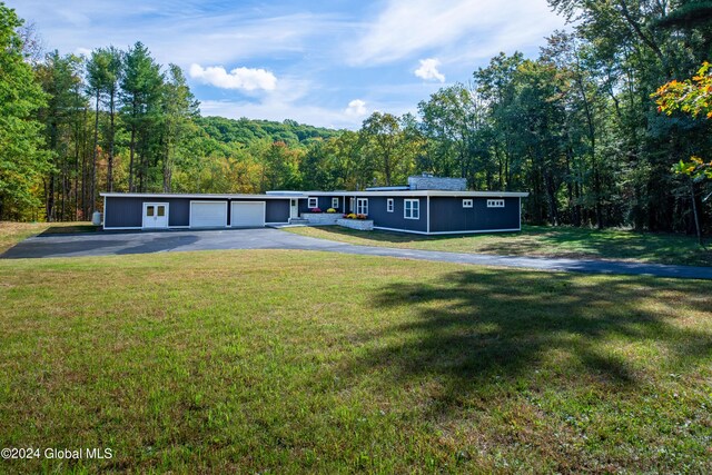 view of front of property with a view of trees, driveway, and a front lawn