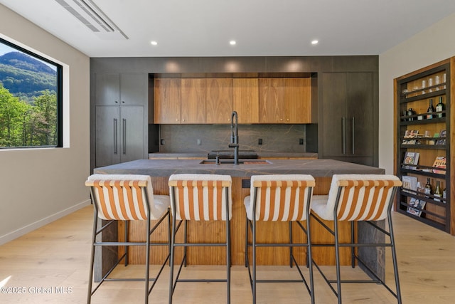 kitchen with a sink, light wood-style flooring, tasteful backsplash, a spacious island, and dark countertops