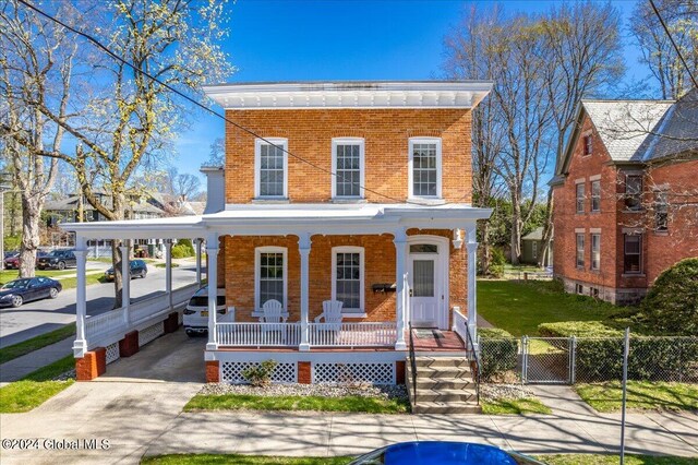 italianate house with a front yard, covered porch, fence, brick siding, and a gate