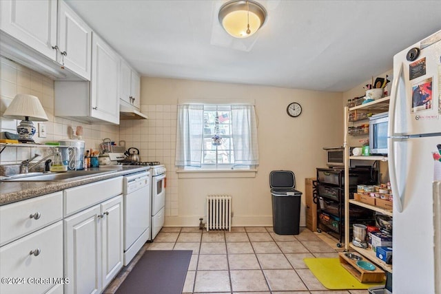 kitchen with white appliances, radiator heating unit, white cabinetry, light tile patterned flooring, and a sink