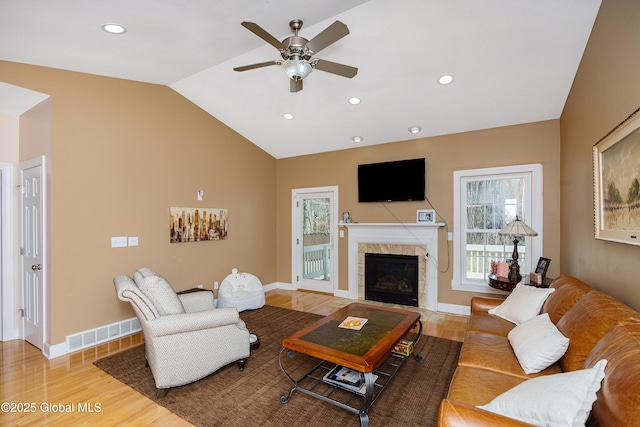 living room with vaulted ceiling, wood finished floors, ceiling fan, a tile fireplace, and visible vents
