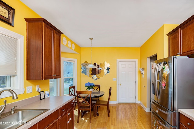 kitchen featuring a sink, stainless steel fridge, light wood-style floors, pendant lighting, and light countertops