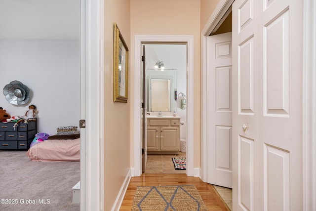 corridor featuring light wood-style flooring, baseboards, and a sink