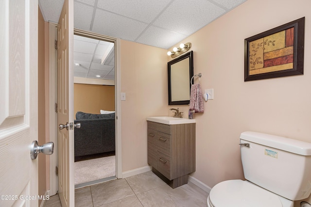 bathroom with tile patterned floors, a drop ceiling, toilet, vanity, and baseboards