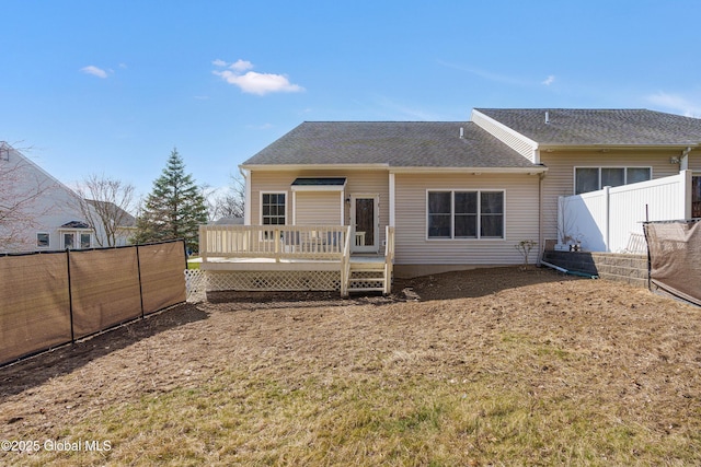 back of property with a wooden deck, roof with shingles, and fence