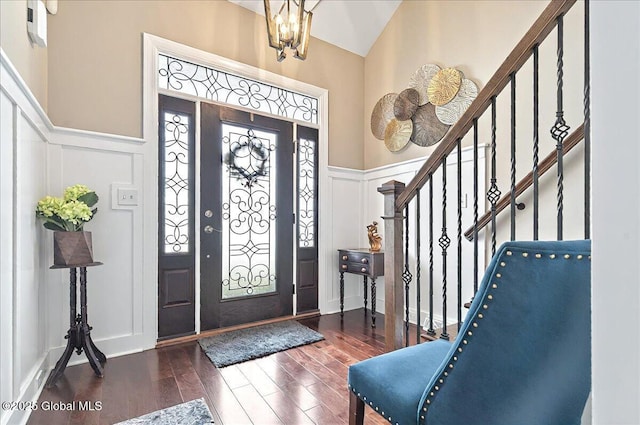 foyer entrance with stairs, wainscoting, wood finished floors, a decorative wall, and a chandelier