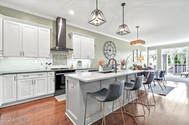 kitchen featuring white cabinets, stainless steel electric range, a sink, wall chimney exhaust hood, and a center island with sink