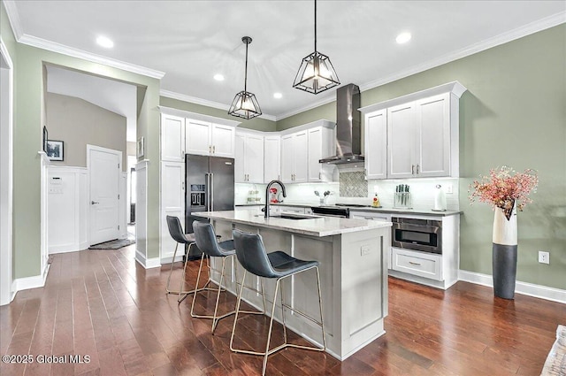kitchen featuring wall chimney range hood, backsplash, a kitchen bar, a sink, and stainless steel appliances