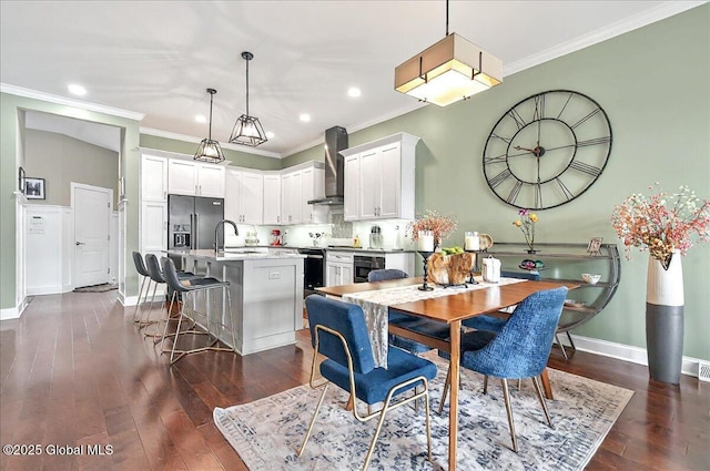 kitchen with ornamental molding, wall chimney range hood, recessed lighting, a sink, and dark wood finished floors