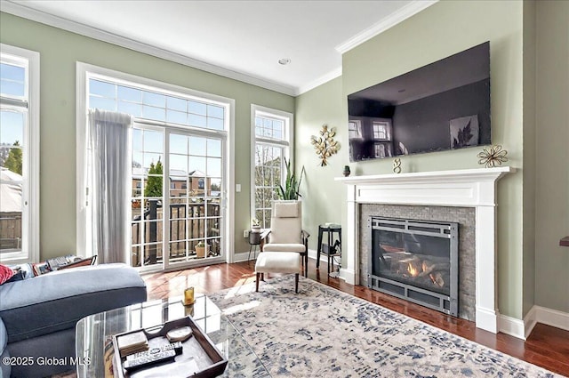 living room with baseboards, ornamental molding, a glass covered fireplace, and wood finished floors