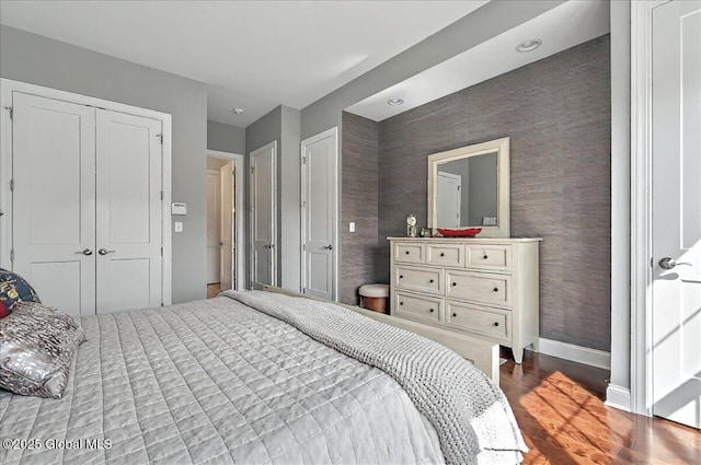 bedroom with baseboards, wallpapered walls, wood finished floors, and a closet