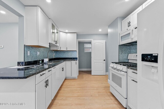 kitchen with light wood-style floors, white appliances, a peninsula, white cabinets, and a sink