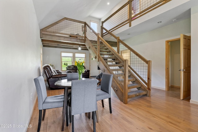 dining room featuring light wood-style floors, stairs, baseboards, and high vaulted ceiling
