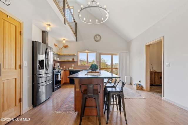 kitchen featuring dark countertops, light wood-type flooring, high vaulted ceiling, stainless steel fridge, and range with gas stovetop