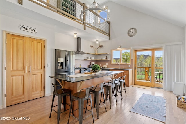 kitchen featuring a sink, high vaulted ceiling, light wood-style floors, and wall chimney exhaust hood