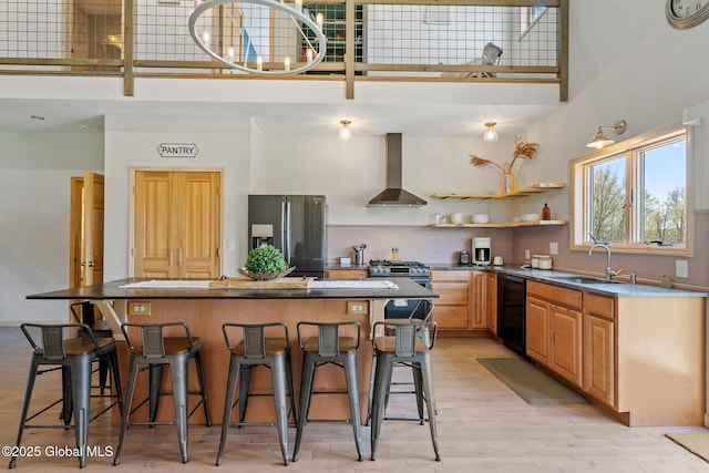 kitchen with wall chimney range hood, a high ceiling, a sink, black dishwasher, and stainless steel refrigerator with ice dispenser