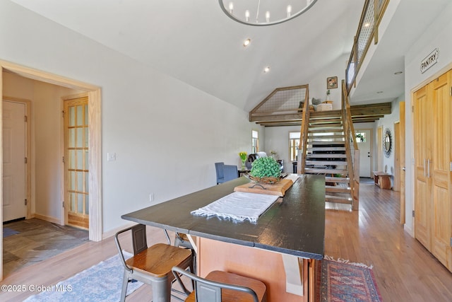 dining space with an inviting chandelier, baseboards, high vaulted ceiling, stairway, and light wood-style flooring