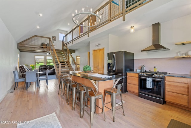 kitchen with dark countertops, high vaulted ceiling, wall chimney range hood, stainless steel range with gas cooktop, and fridge with ice dispenser