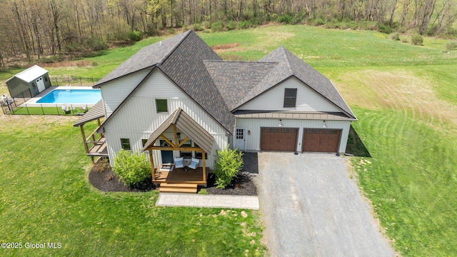 view of front of house featuring a front lawn, gravel driveway, roof with shingles, a fenced in pool, and an attached garage