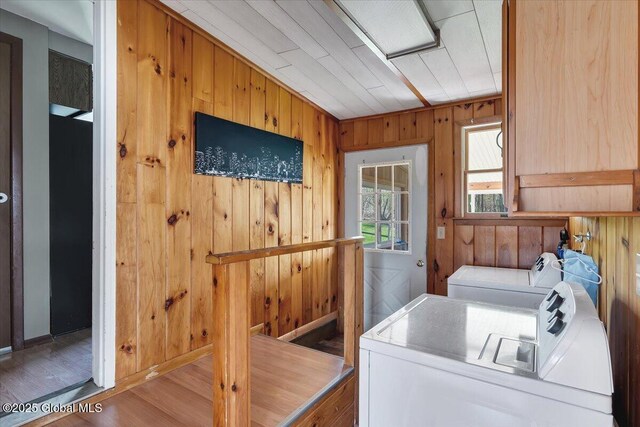 laundry area featuring laundry area, washing machine and dryer, wood walls, wood finished floors, and baseboards