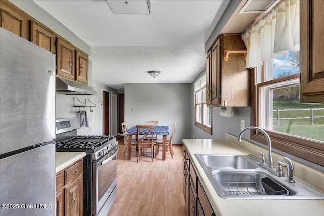 kitchen featuring brown cabinets, a sink, light countertops, stainless steel appliances, and under cabinet range hood
